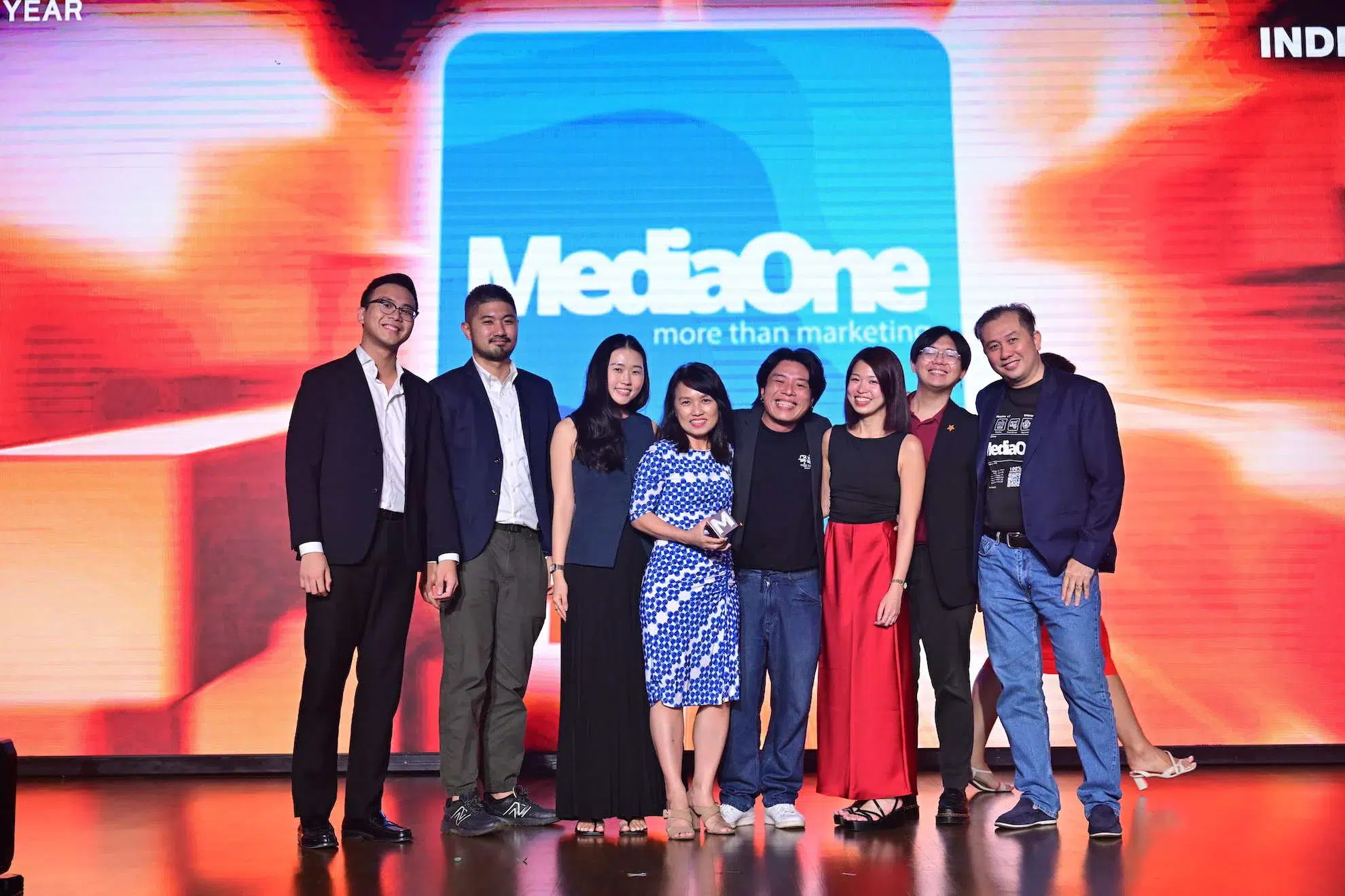 MediaOne team celebrating on stage with an award, standing in front of a screen displaying the 'MediaOne more than marketing' logo.